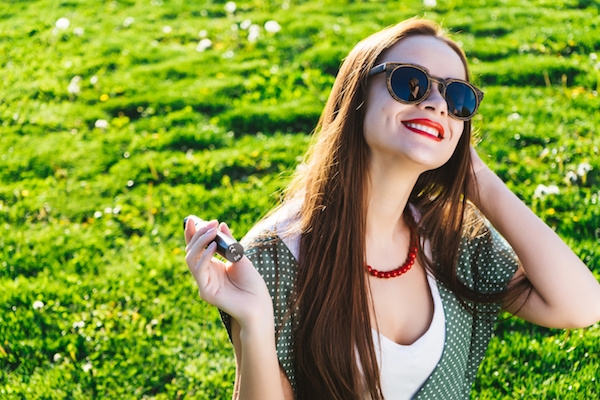 happy girl enjoying her vape outside with green grass in the background